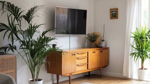 Un salon avec un meuble en bois, un téléviseur à écran plat et plusieurs plantes en pot.