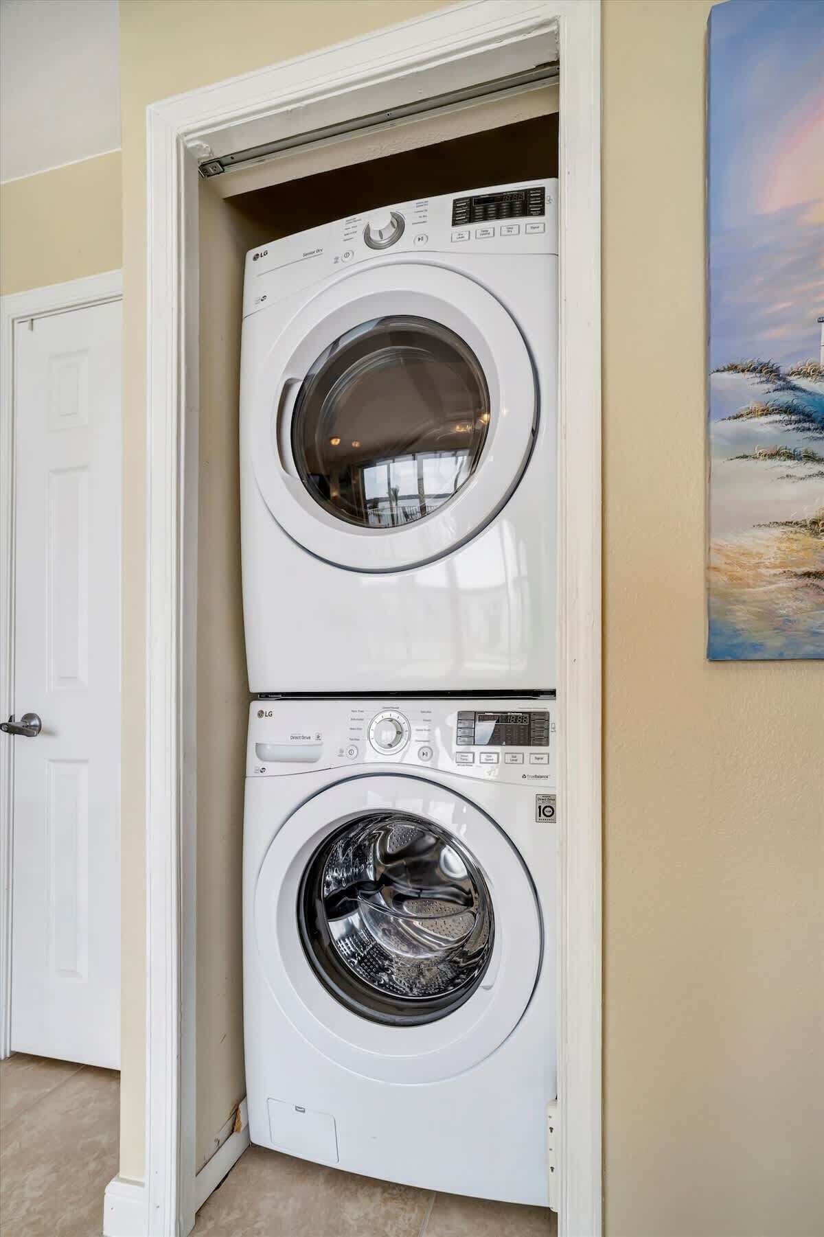 Una lavadora y secadora apiladas en un cuarto de lavado, con una puerta y un cuadro en la pared.