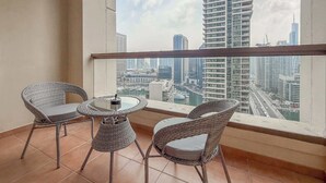 Ein Balkon mit Korbstühlen und einem kleinen Tisch, mit Blick auf eine Stadtlandschaft mit hohen Gebäuden und einem Yachthafen.