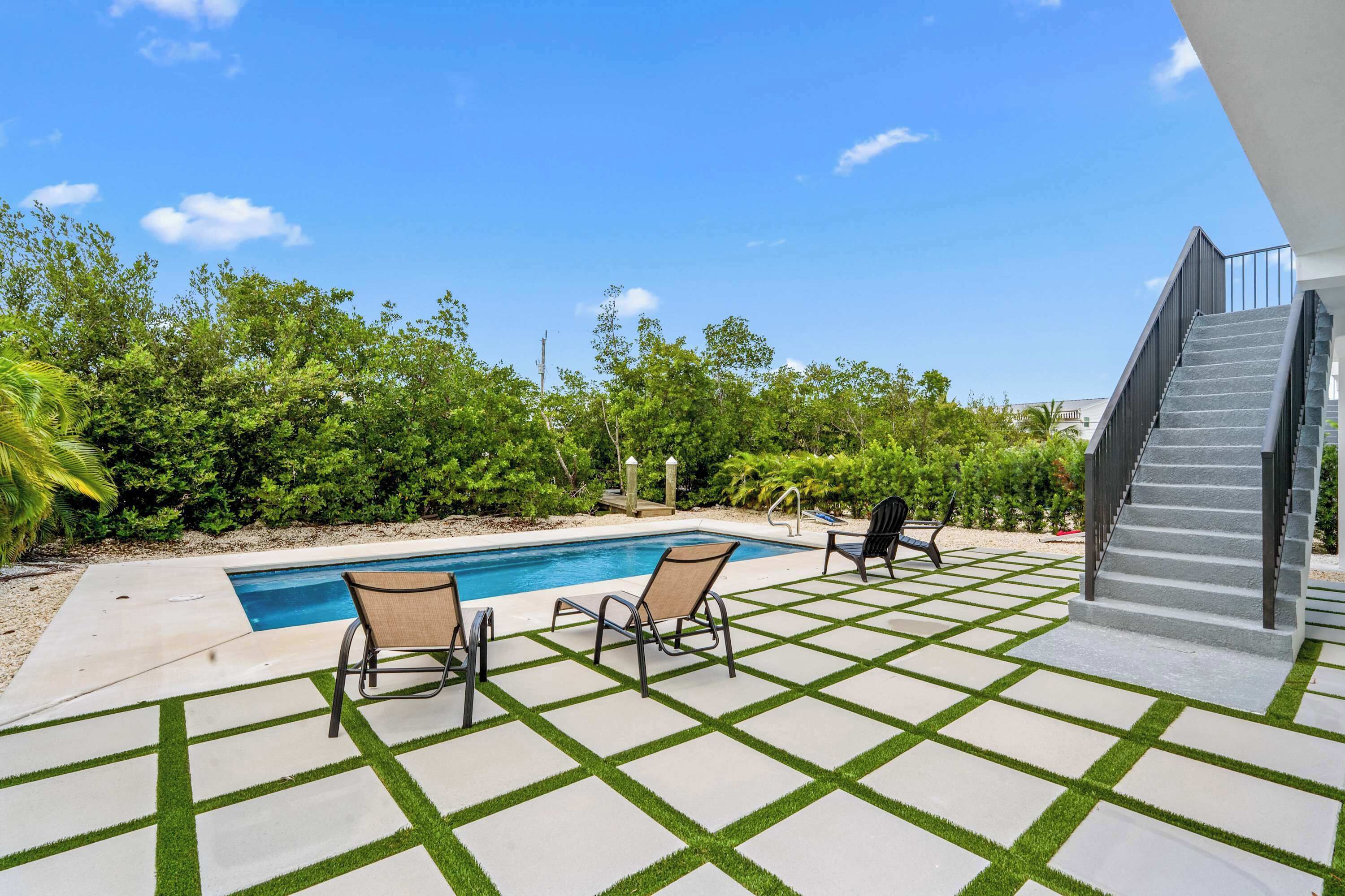 A pool area with two lounge chairs and a staircase leading to an upper level.