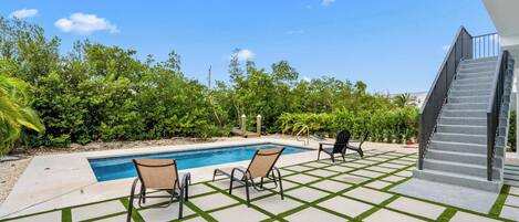 A pool area with two lounge chairs and a staircase leading to an upper level.