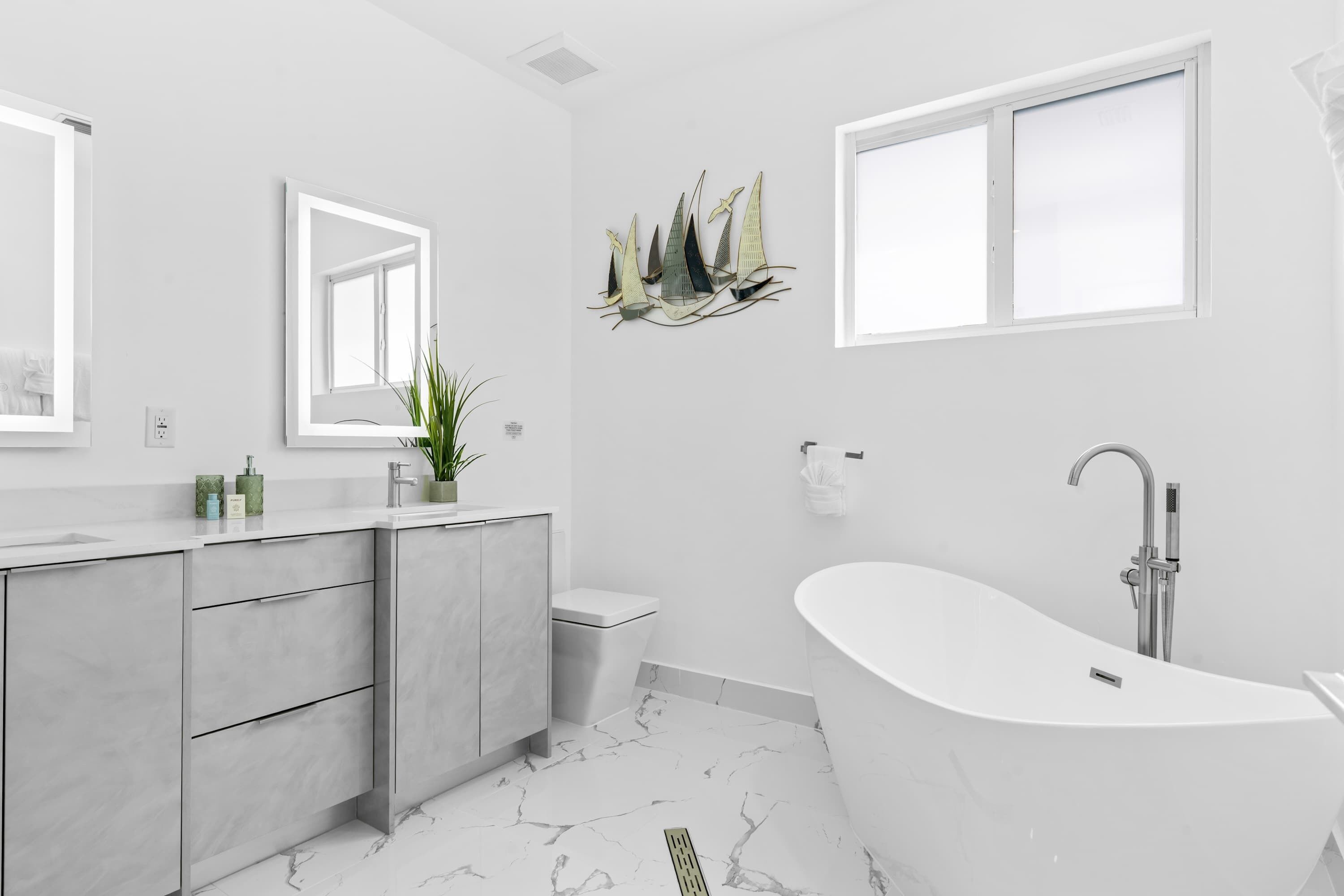 A modern bathroom with a freestanding bathtub, a large mirror, and a decorative wall piece.