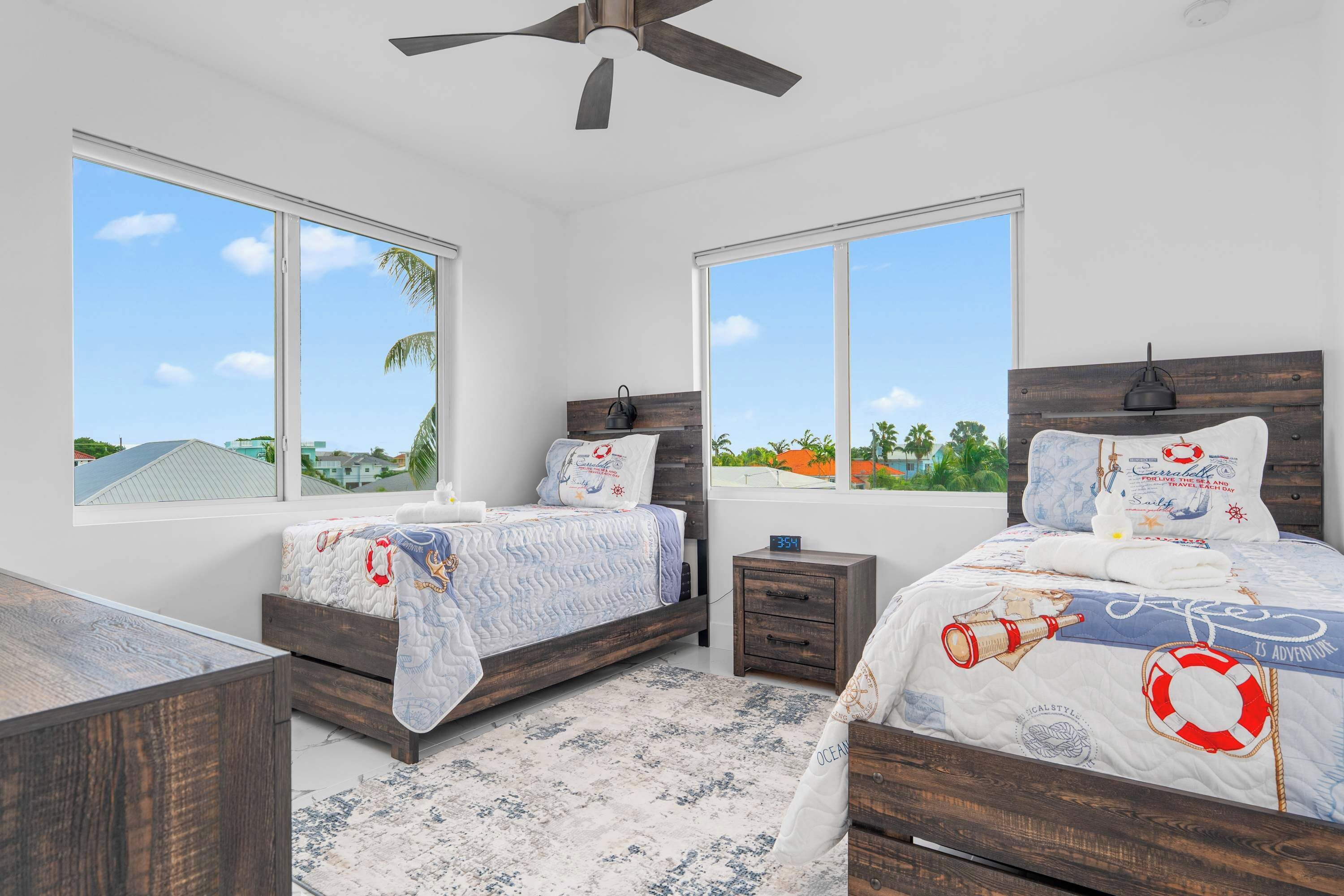 A bedroom with two beds, large windows, a ceiling fan, and a view of the outdoors.