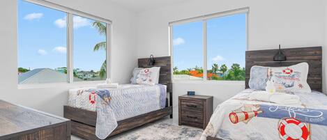 A bedroom with two beds, large windows, a ceiling fan, and a view of the outdoors.