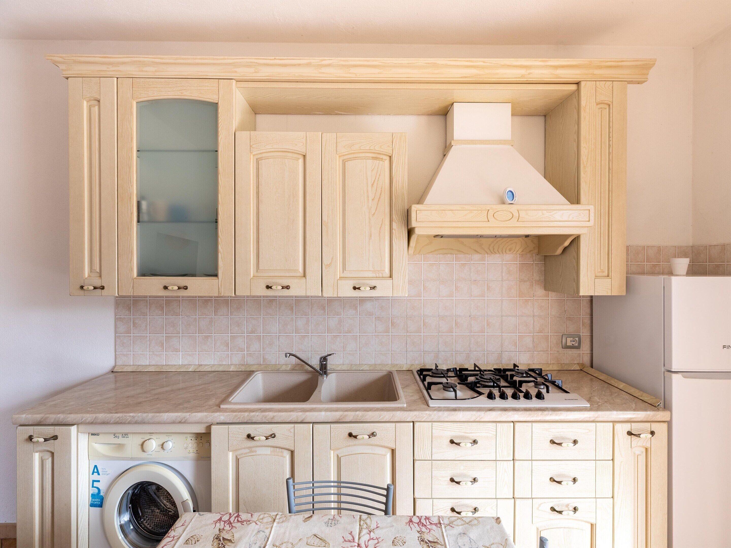 A kitchen with wooden cabinets, a washing machine, a sink, and a stove.