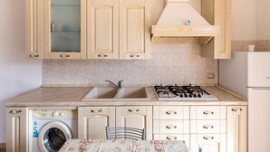 A kitchen with wooden cabinets, a washing machine, a sink, and a stove. - In a Residence With a Private Patio and air Conditioning (Castelsardo)