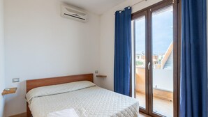 A bedroom with a bed, a window with curtains, a ceiling air conditioner, and a view of buildings outside. - In a Residence With a Private Patio and air Conditioning (Castelsardo)