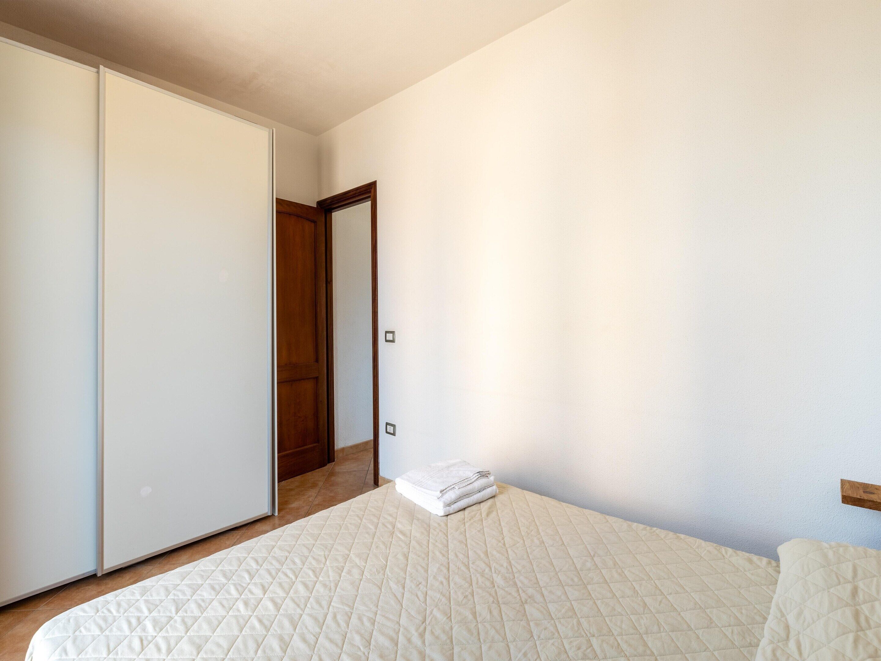Een slaapkamer met een bed, een kledingkast en een deur naar een andere kamer.