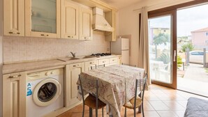 A compact kitchen with a washing machine, a dining table with chairs, and a view of the outside. - In a Residence With a Private Patio and air Conditioning (Castelsardo)