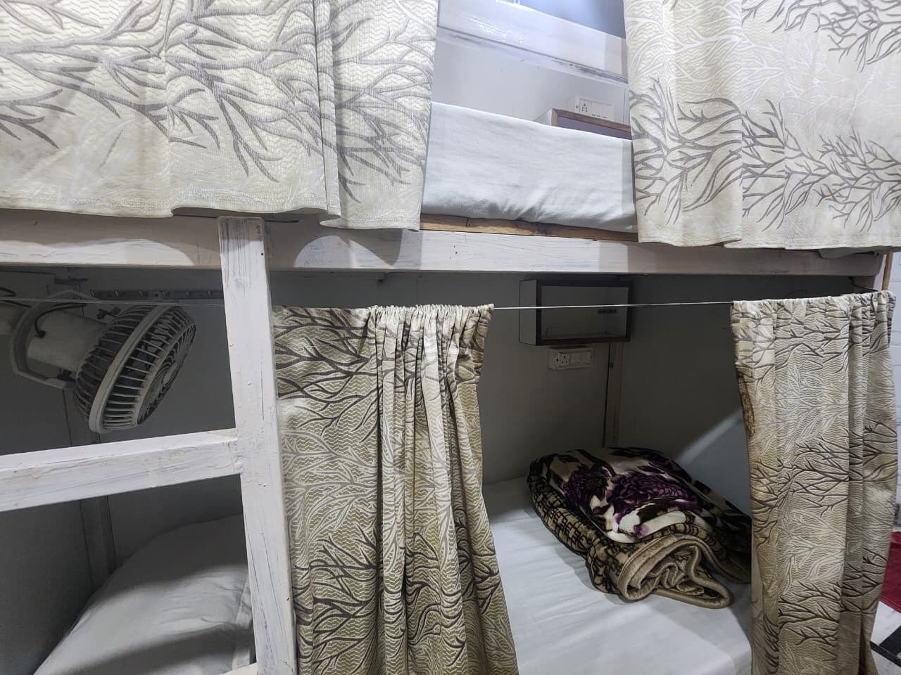 Een stapelbed met een ventilator op het onderbed en een deken op het bovenbed.