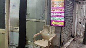 Un hostal con puerta de cristal, una silla de plástico en el exterior y un letrero que anuncia camas en dormitorios con aire acondicionado, habitaciones con y sin aire acondicionado y WiFi gratuito.