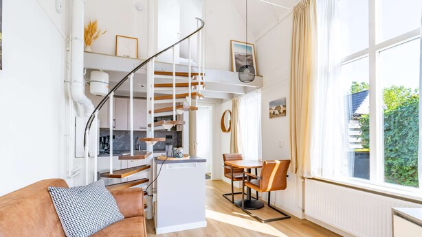 A modern living space with a staircase leading to a loft area, a dining area, and a kitchen. - Charming 2-person Apartment Located Near the Center (De Koog)
