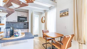 Una cocina moderna con horno empotrado, una zona de comedor con mesa de madera y sillas de cuero, y un espejo grande en la pared.