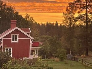 Una casa roja con una ventana y una puerta blancas, rodeada de árboles y una cerca.