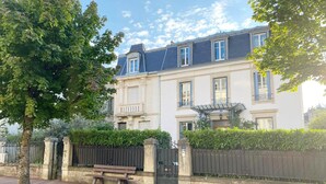 A two-story building with a gated entrance, a bench outside, and a clear sky. - Amazing Holiday Home in the Heart of Vittel (Vittel)