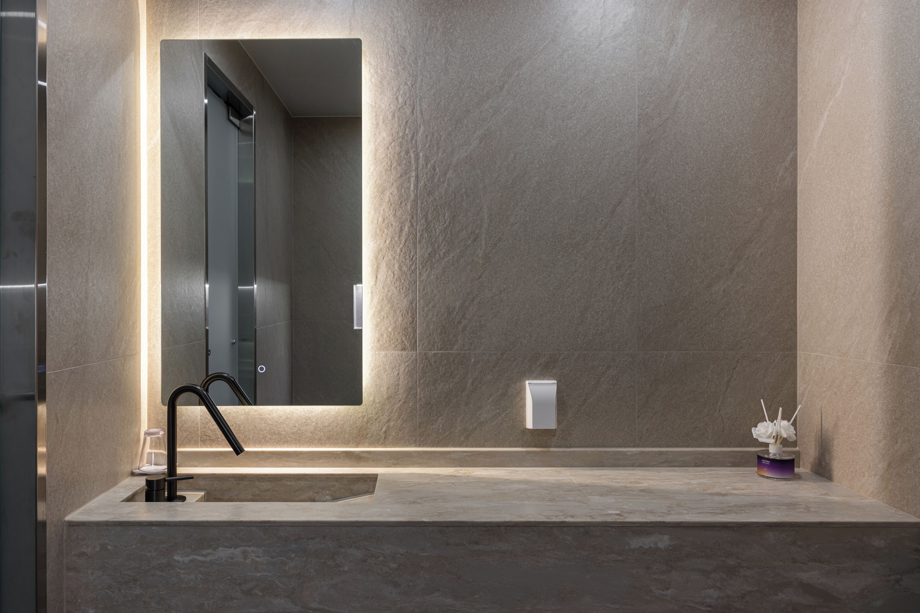 Un bagno moderno con uno specchio grande, un lavandino e un piccolo vaso con fiori.