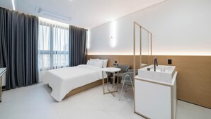 Une chambre d’hôtel moderne comprenant un lit, une petite table, une chaise, un bureau, un miroir et une salle de bain avec un lavabo.