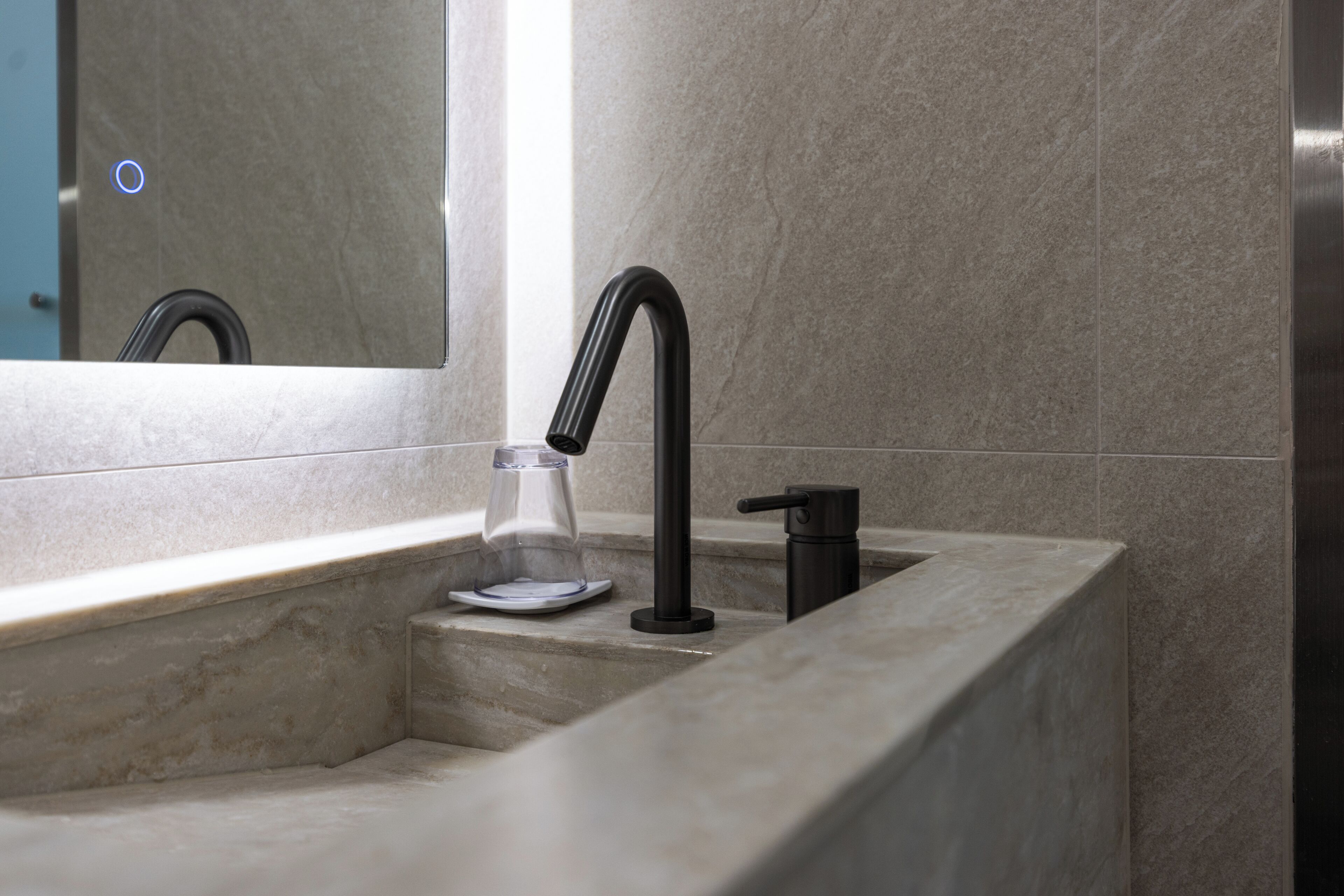 A modern bathroom with a marble sink, a black faucet, and a glass soap dispenser.