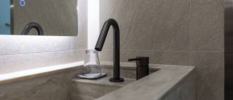A modern bathroom with a marble sink, a black faucet, and a glass soap dispenser.