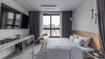 Una habitación de hotel moderna con cama, mesita de noche y un amplio ventanal con cortinas.