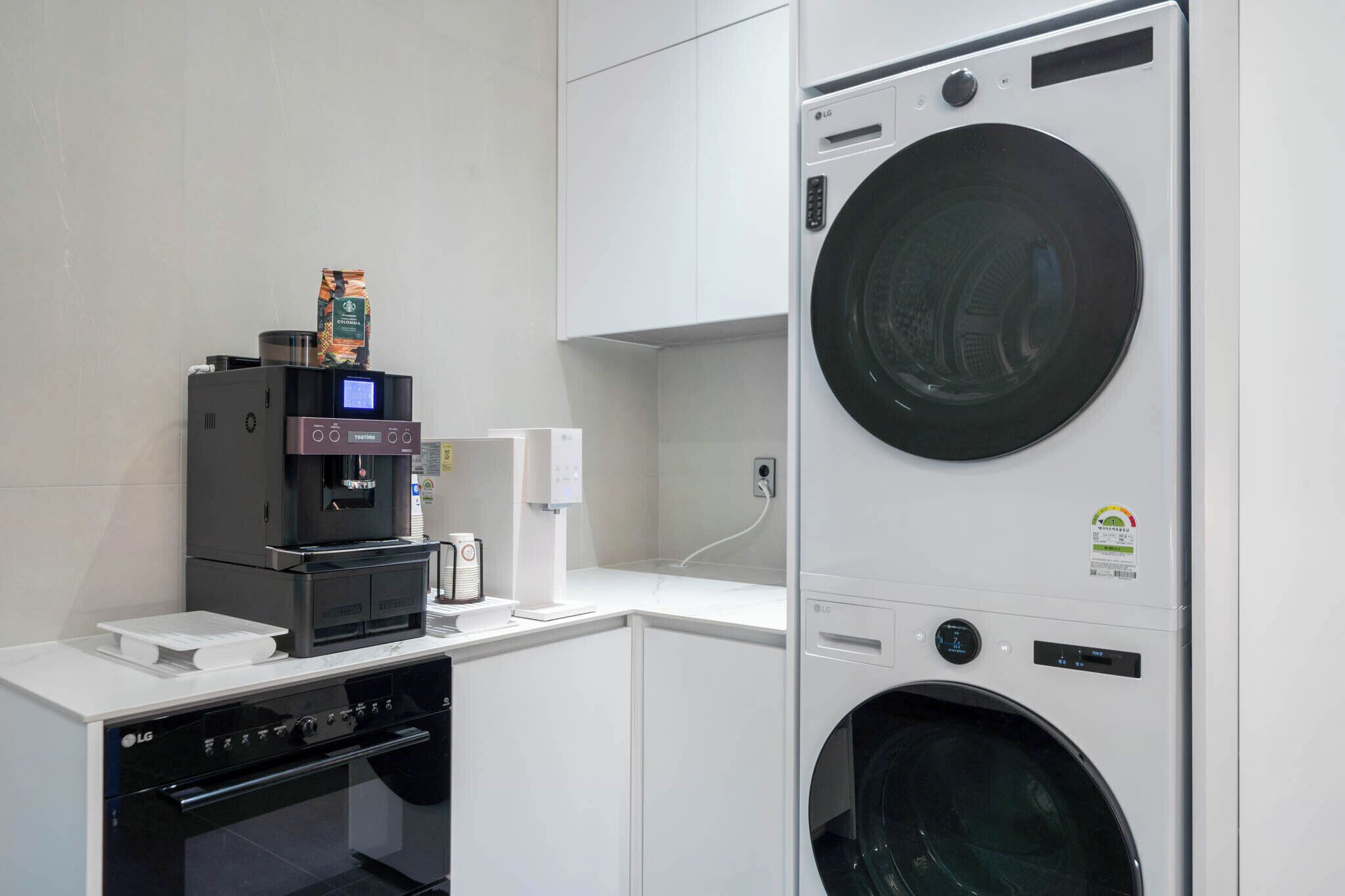 Een compacte keuken met een LG koffieapparaat, een magnetron en een ingebouwde was- en droogmachine.
