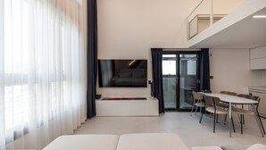 Un salon moderne avec un téléviseur à écran plat fixé au mur, un coin repas avec une table et des chaises, et un canapé au premier plan.