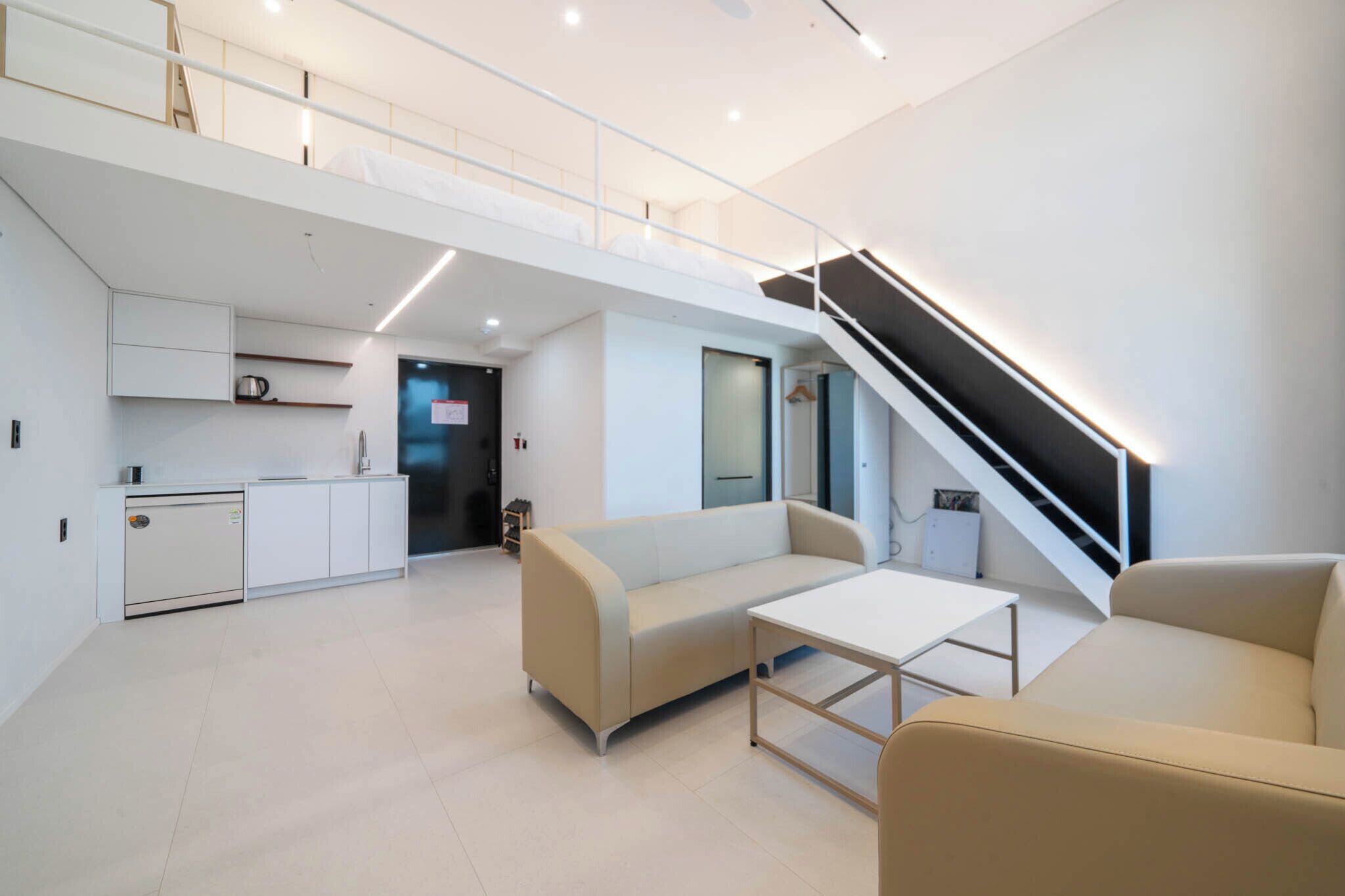 Un espacio habitable moderno y abierto con cocina, sofá, mesa de centro y una escalera.