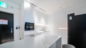 Une cuisine moderne avec des meubles blancs, un plan de travail en marbre, un four encastré et un réfrigérateur noir.