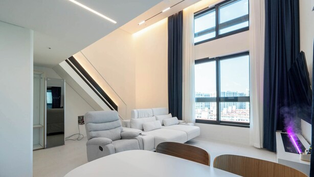 Un salon moderne avec un canapé blanc, une table à manger et une grande fenêtre avec des rideaux.