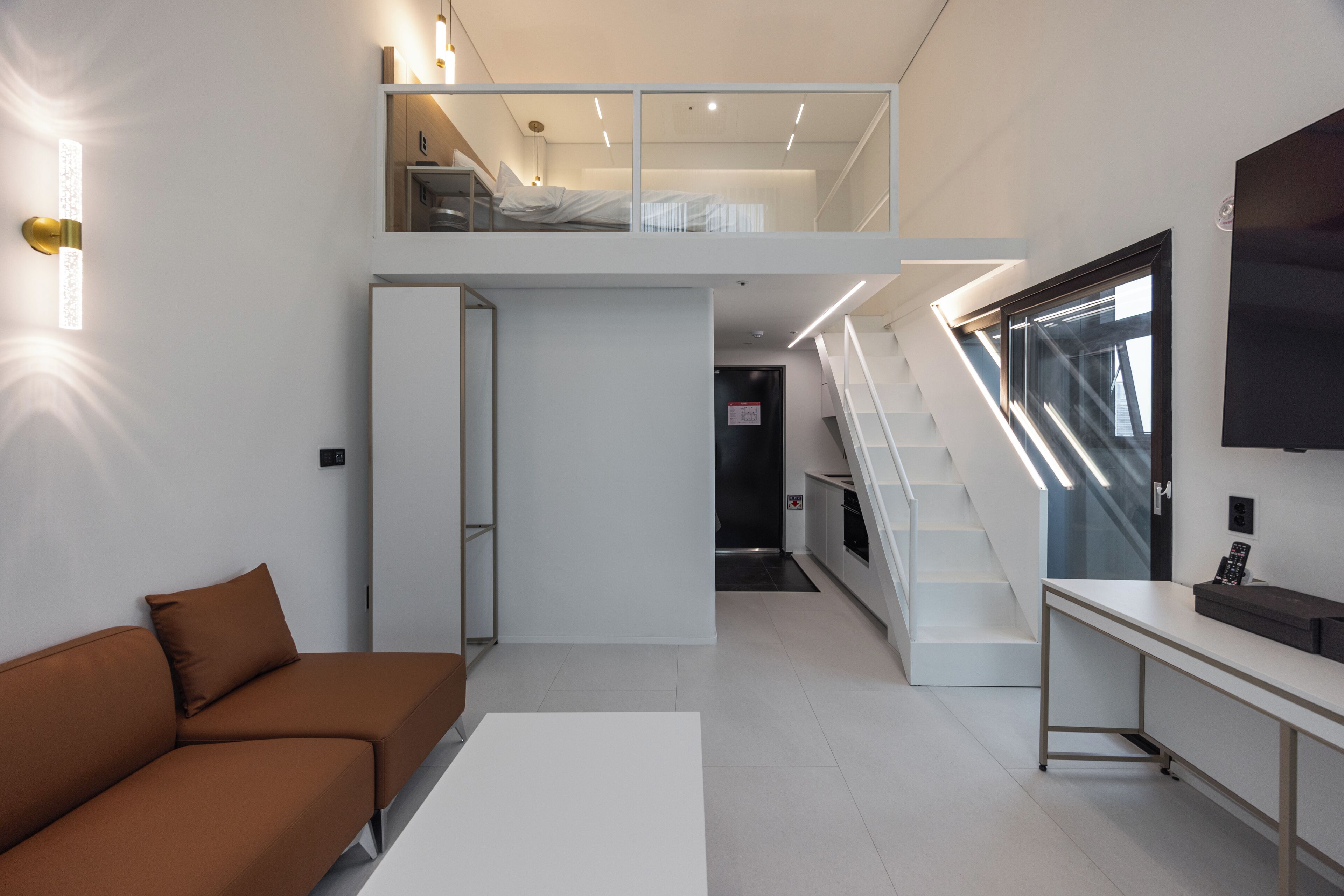 A modern interior with a sofa, a desk, a staircase, and a TV.