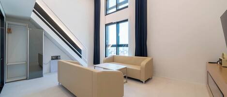 Ein modernes Hotelzimmer mit einer Treppe, zwei Sofas, einem kleinen Tisch und einem großen Fenster mit Vorhängen.