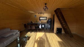 Un interior de cabaña acogedor, con paredes de madera, una zona de comedor, un sofá y una escalera.