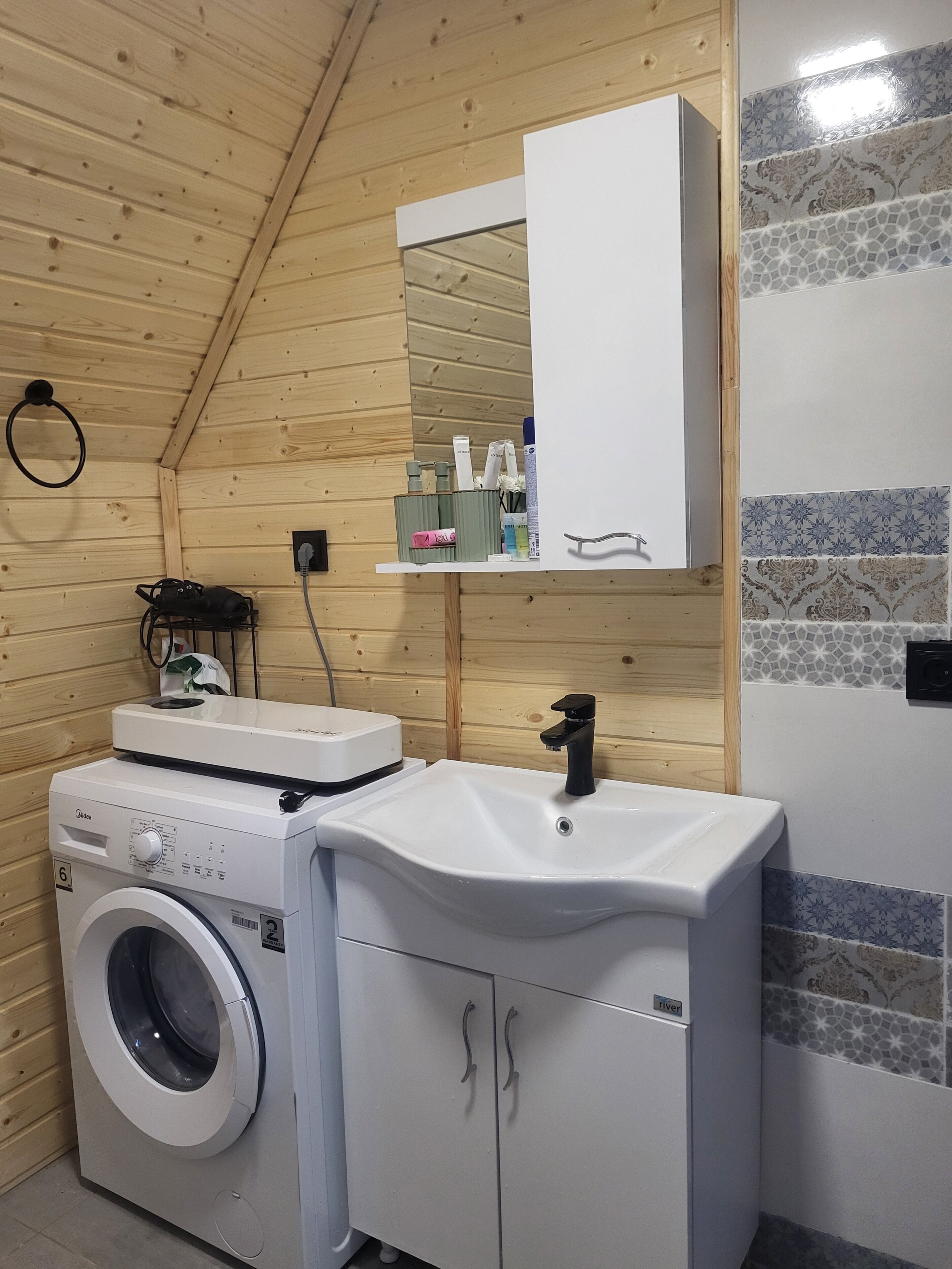 Ein kleines Badezimmer mit Waschmaschine, Waschbecken und Spiegel darüber.