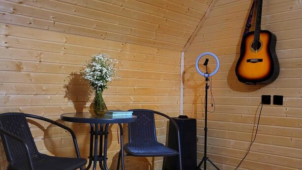 A cozy room with a wooden ceiling, a guitar hanging on the wall, a table with chairs, and a speaker. - Svanieri cozy cottage in the mountains (Mestia Municipality)