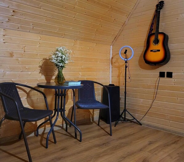 A cozy room with a wooden ceiling, a guitar hanging on the wall, a table with chairs, and a speaker.