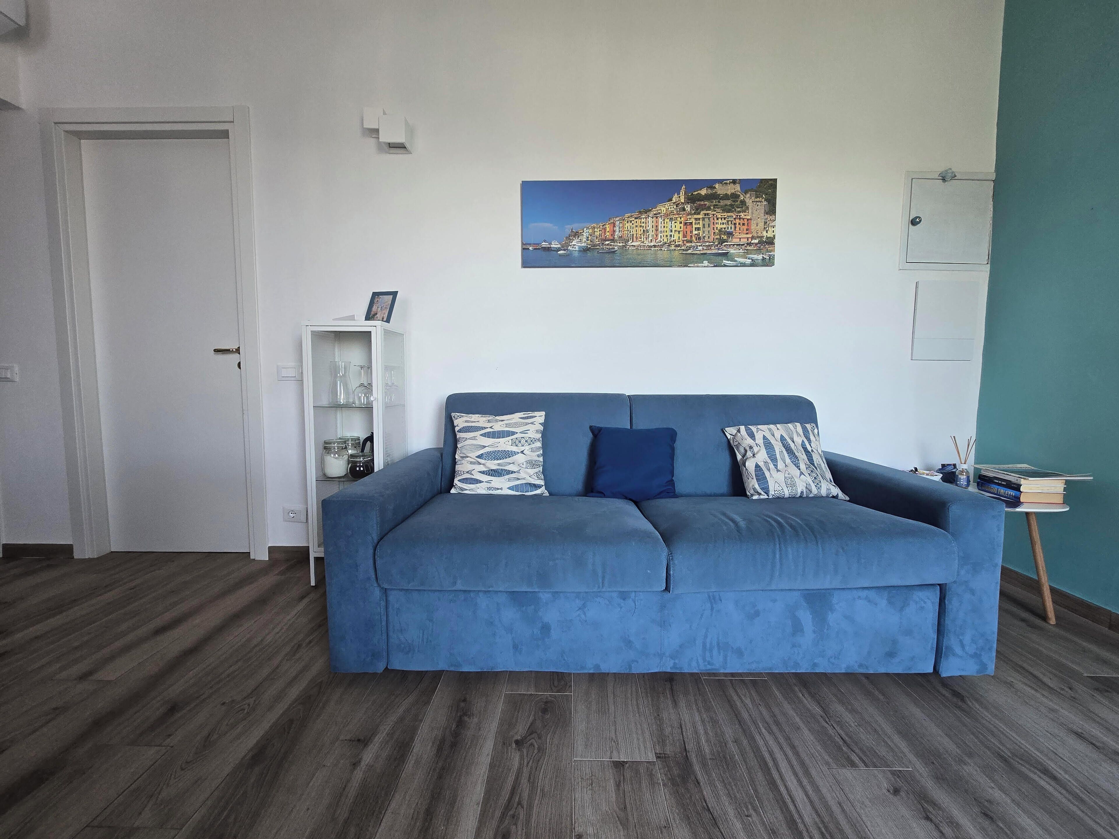 Un salon moderne avec un canapé bleu, un tableau représentant une ville côtière et un plancher en bois.