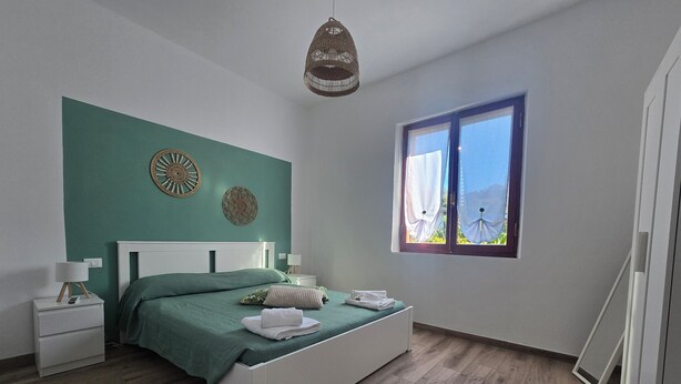 Un dormitorio con cama, mesitas de noche, una ventana y decoración en la pared.