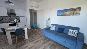 Una sala moderna con un sofá azul, una mesa de comedor con sillas y una zona de cocina con armarios blancos.