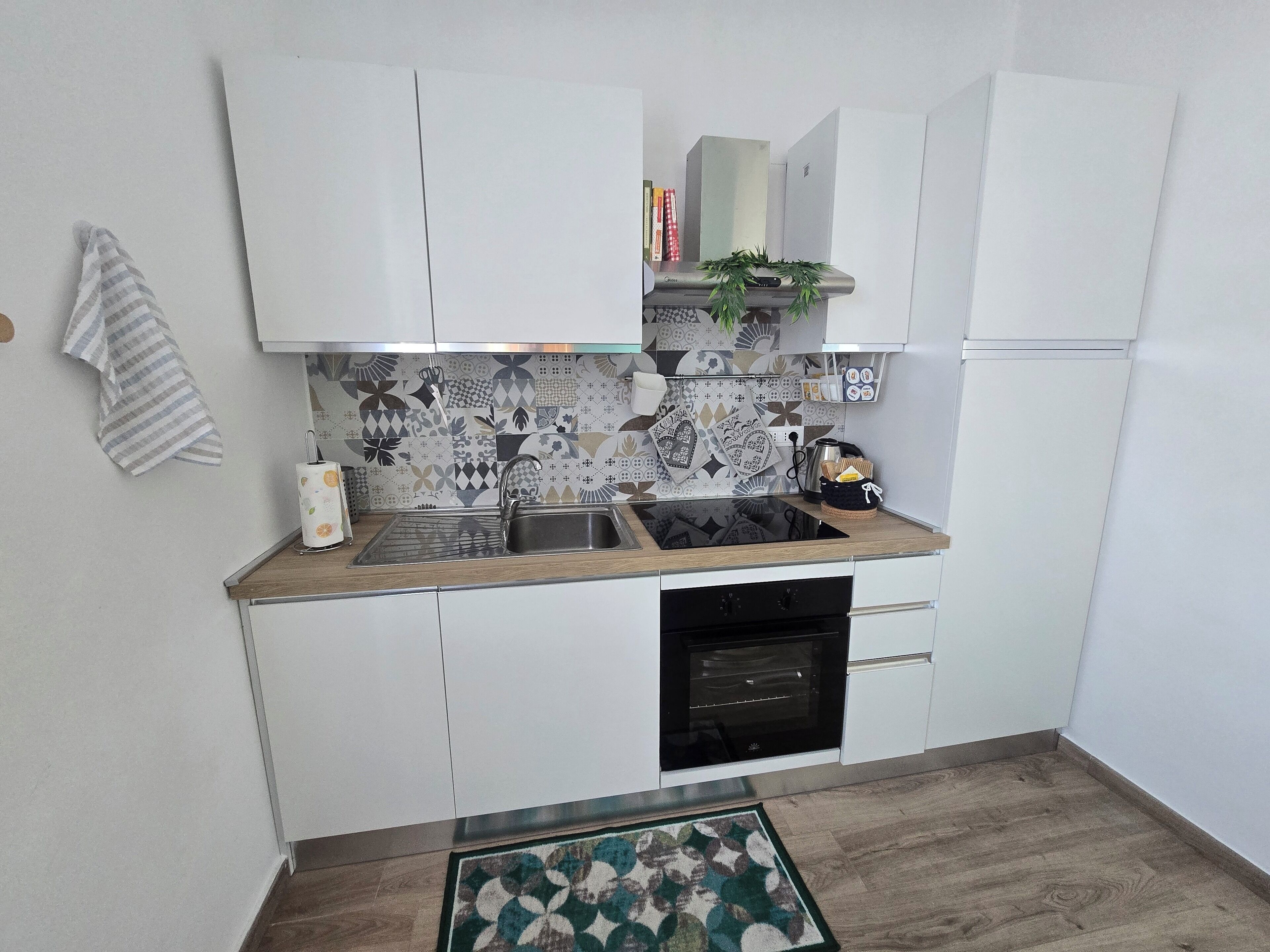 A compact kitchen with white cabinets, a stainless steel sink, a built-in oven, and a patterned backsplash.