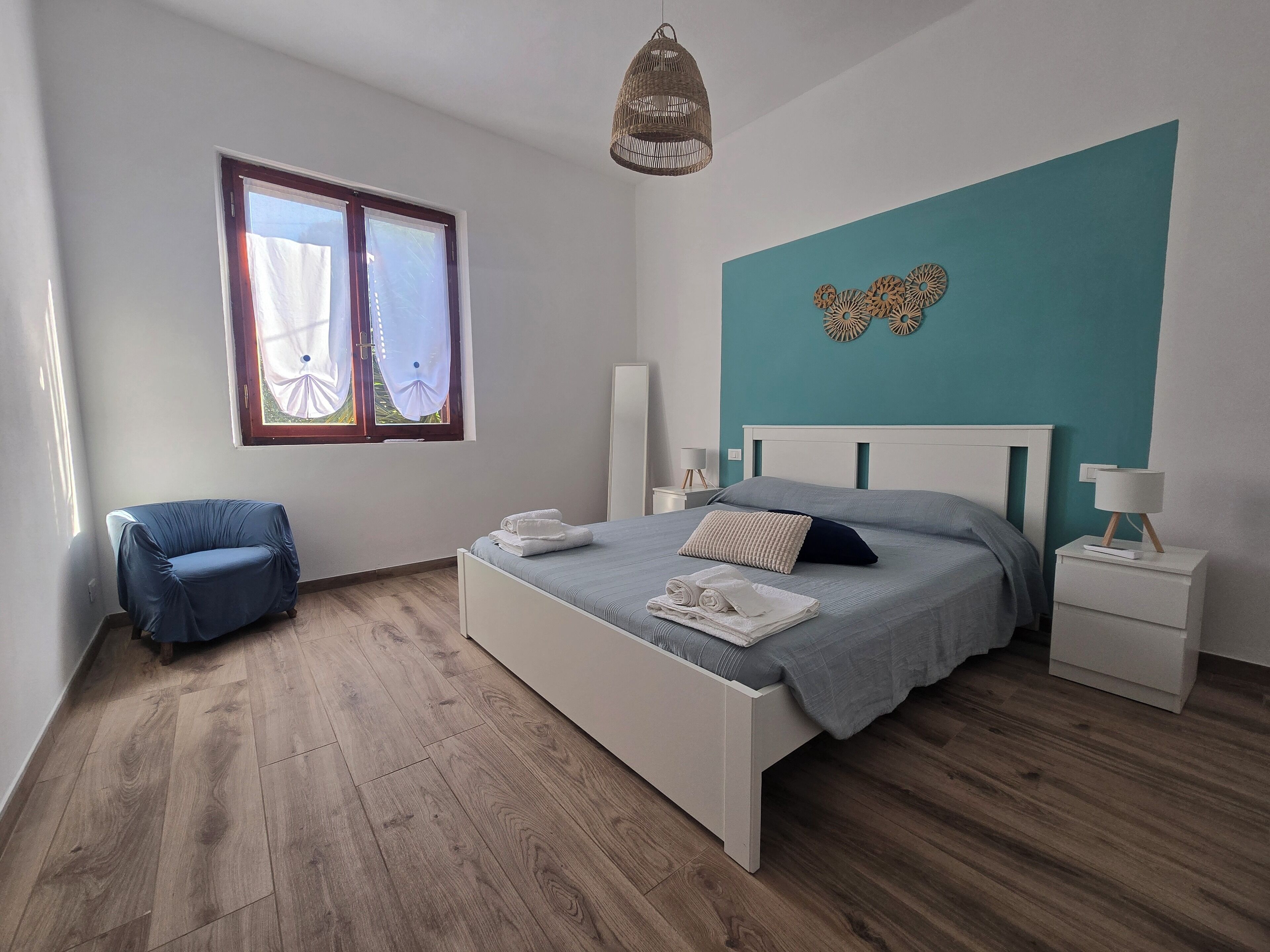 Une chambre à coucher avec un lit, une chaise, une table de chevet, une lampe et une fenêtre avec des rideaux.