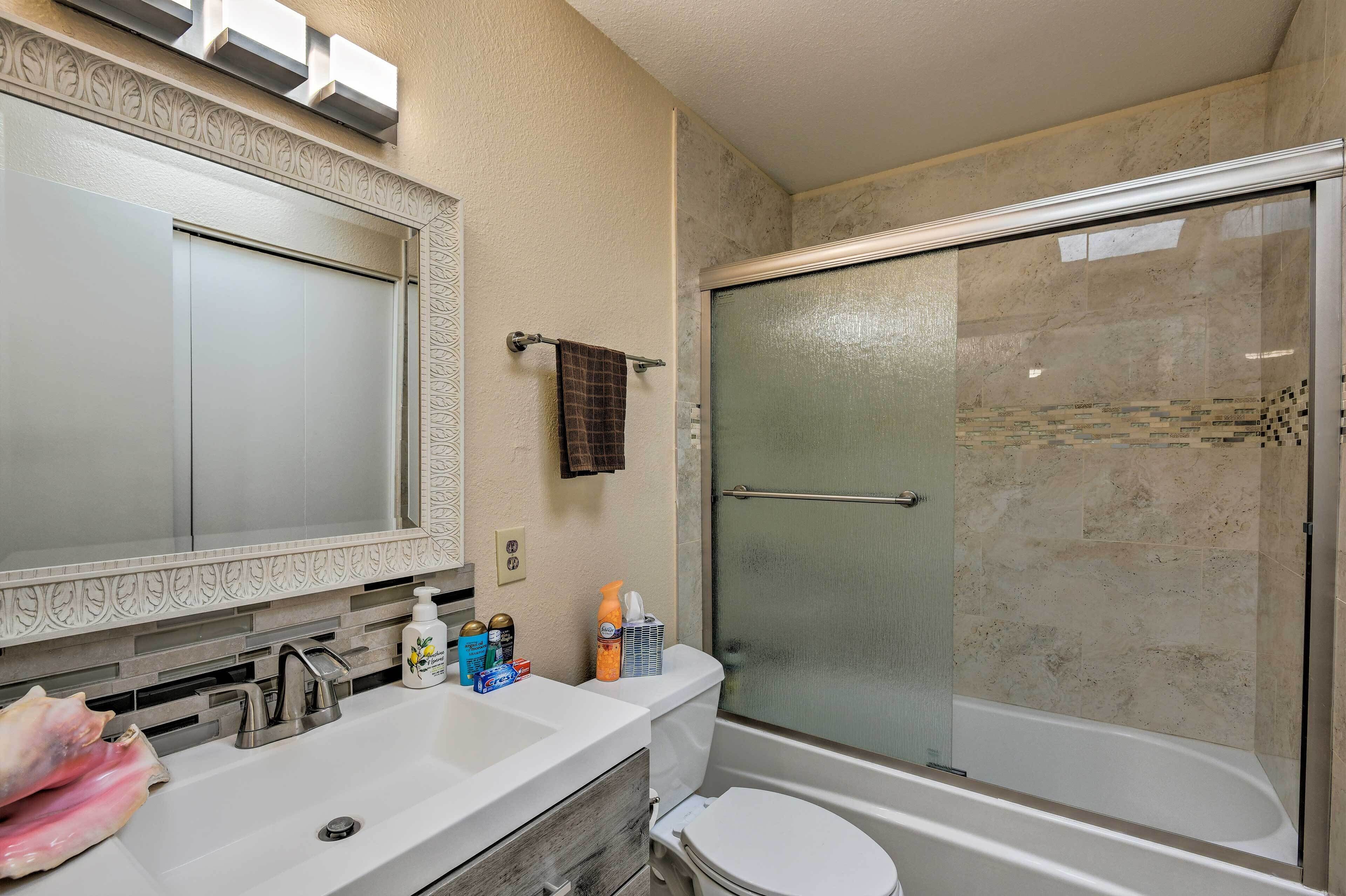 A bathroom with a large mirror, a sink with toiletries, a toilet, and a glass-enclosed shower.
