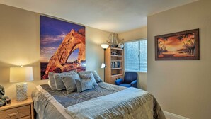 Een slaapkamer met een groot bed, een nachtkastje, een lamp, een boekenkast, een stoel en een raam met jaloezieën.