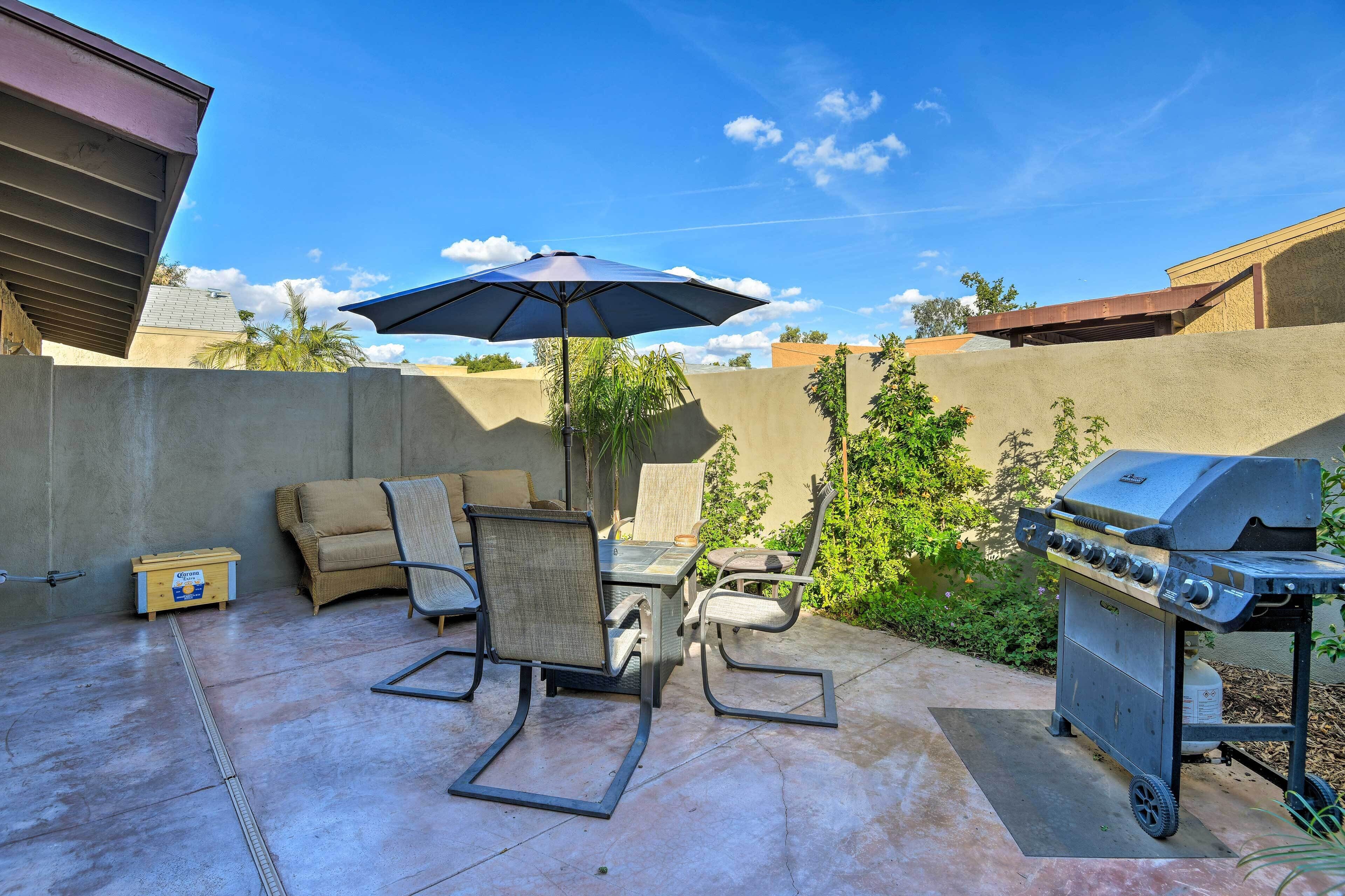 An outdoor patio with a grill, seating, and a table under a large umbrella.