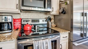 Una cocina moderna con electrodomésticos de acero inoxidable, incluyendo un microondas, horno y refrigerador. Hay una cafetera y un hervidor rojo sobre la encimera.