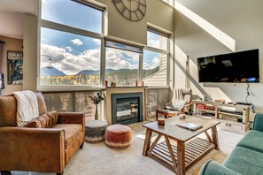 Un amplio salón con ventanas grandes, una chimenea, un televisor y una zona de estar acogedora.