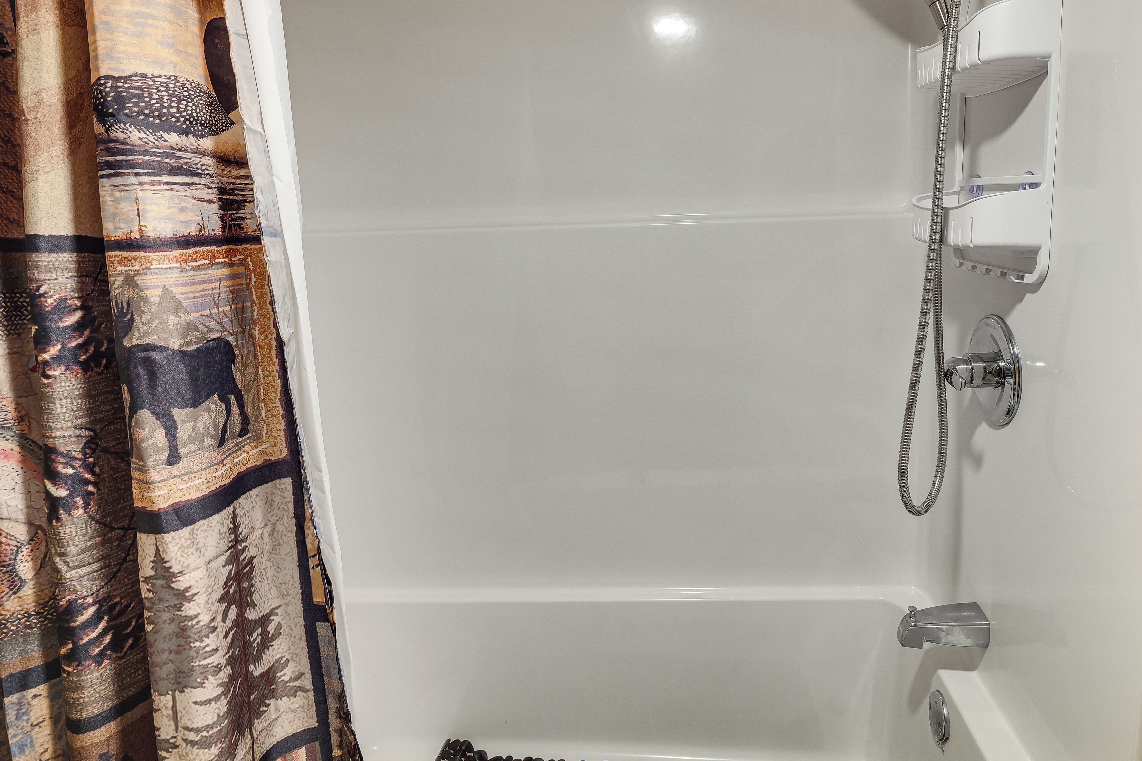A bathroom with a bathtub, shower, and a curtain with a forest and animal print.
