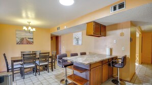 Una cocina con una isla central, taburetes de bar, una mesa de comedor con sillas y una lámpara colgante.