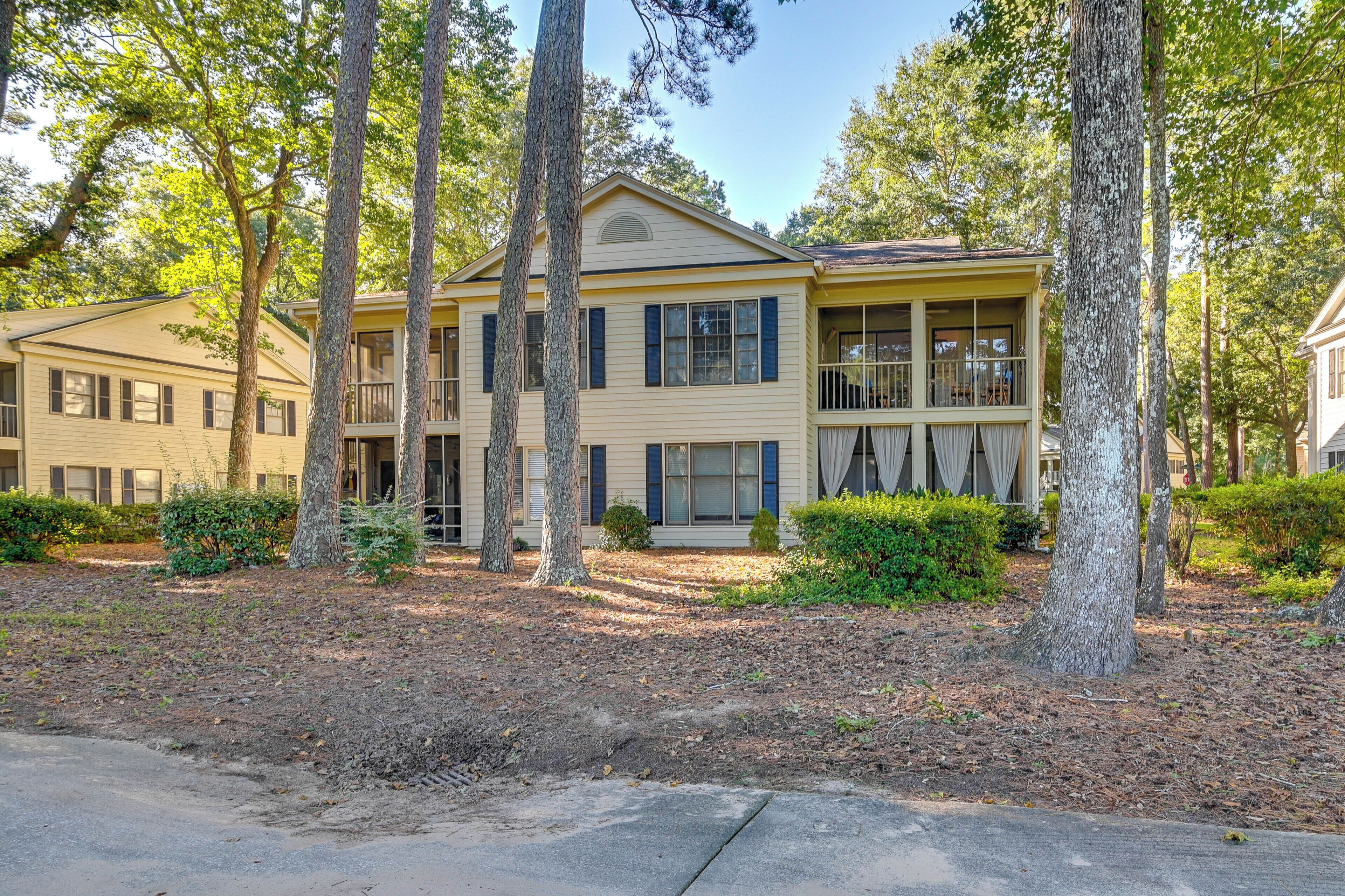 A two-story building with a beige exterior and dark shutters, surrounded by trees and a landscaped yard.