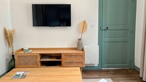 Ett vardagsrum med ett TV-bord i trä, en platt-TV, en grön dörr och ett litet bord med tidningar.