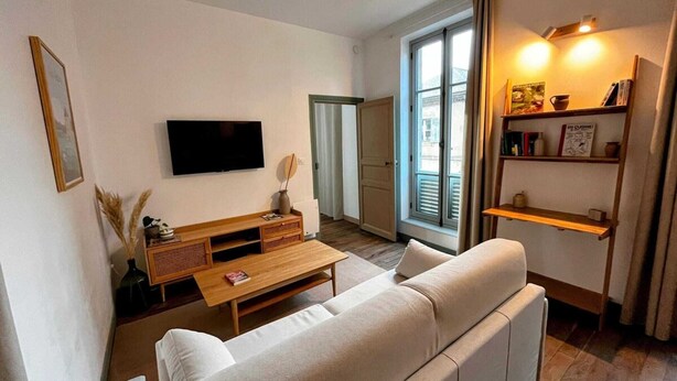 Ett modernt vardagsrum med en soffa, ett soffbord i trä, en platt-TV och en bokhylla.